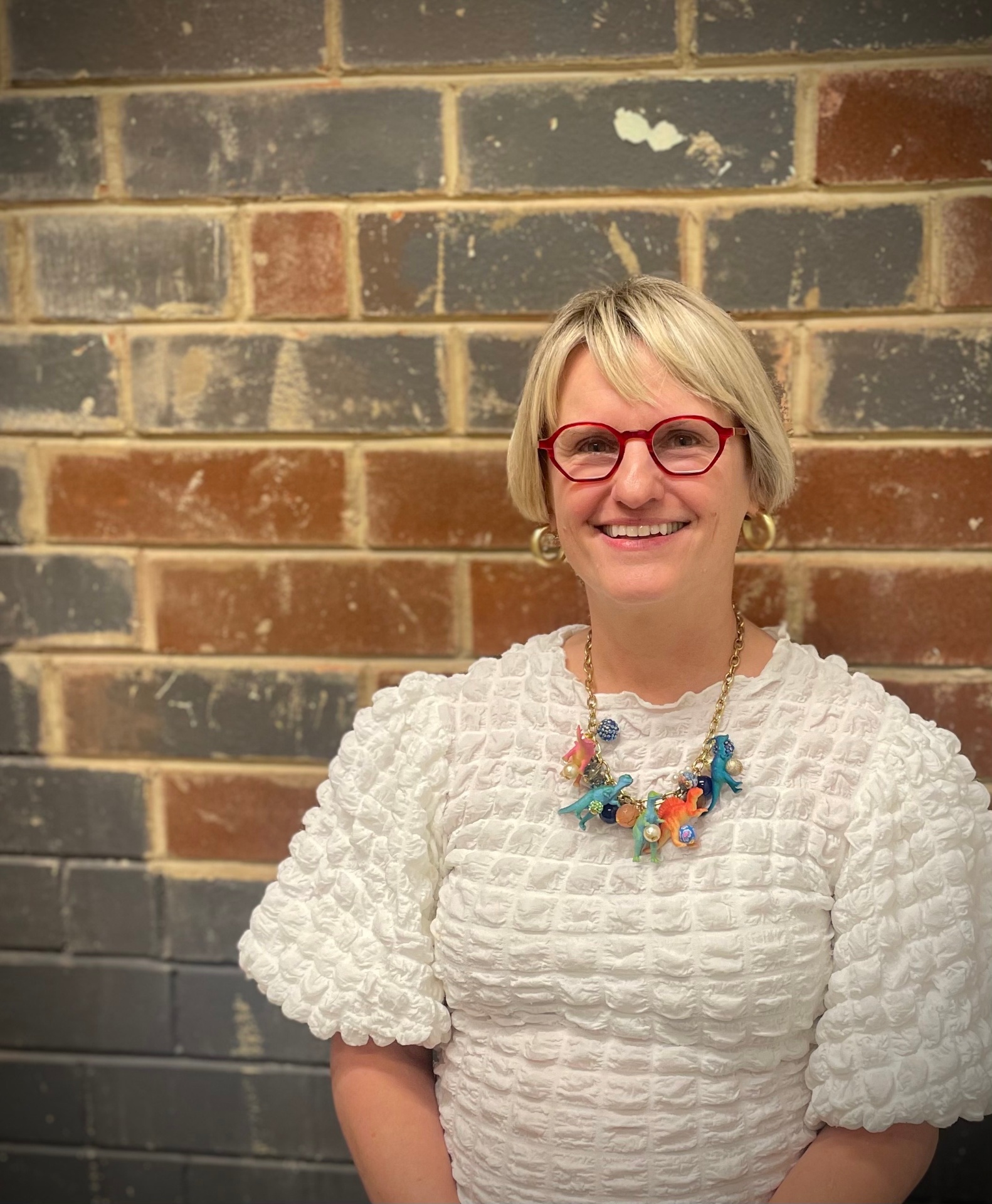 Wendy Ward Osborn, smiling, in red glasses and a white textured top